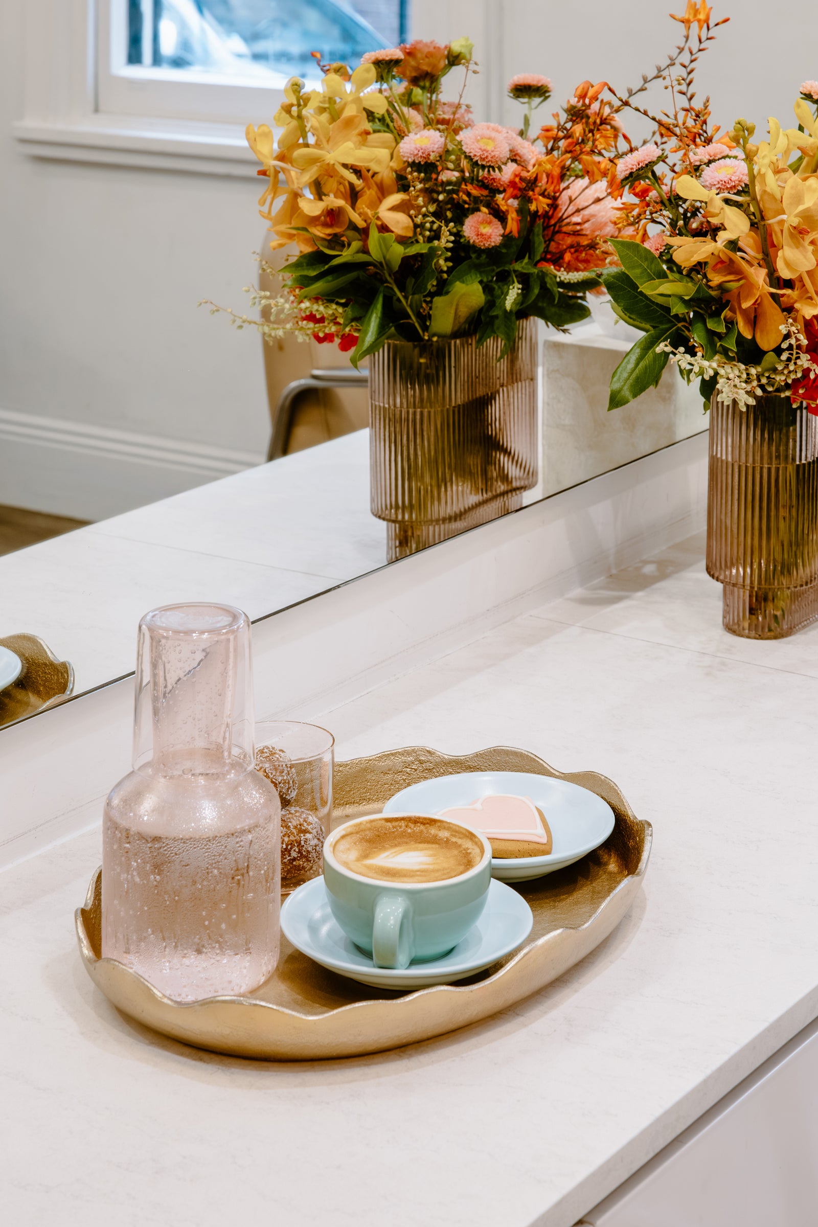 Café setting with a tray of coffee, a carafe, and flowers on a white surface.