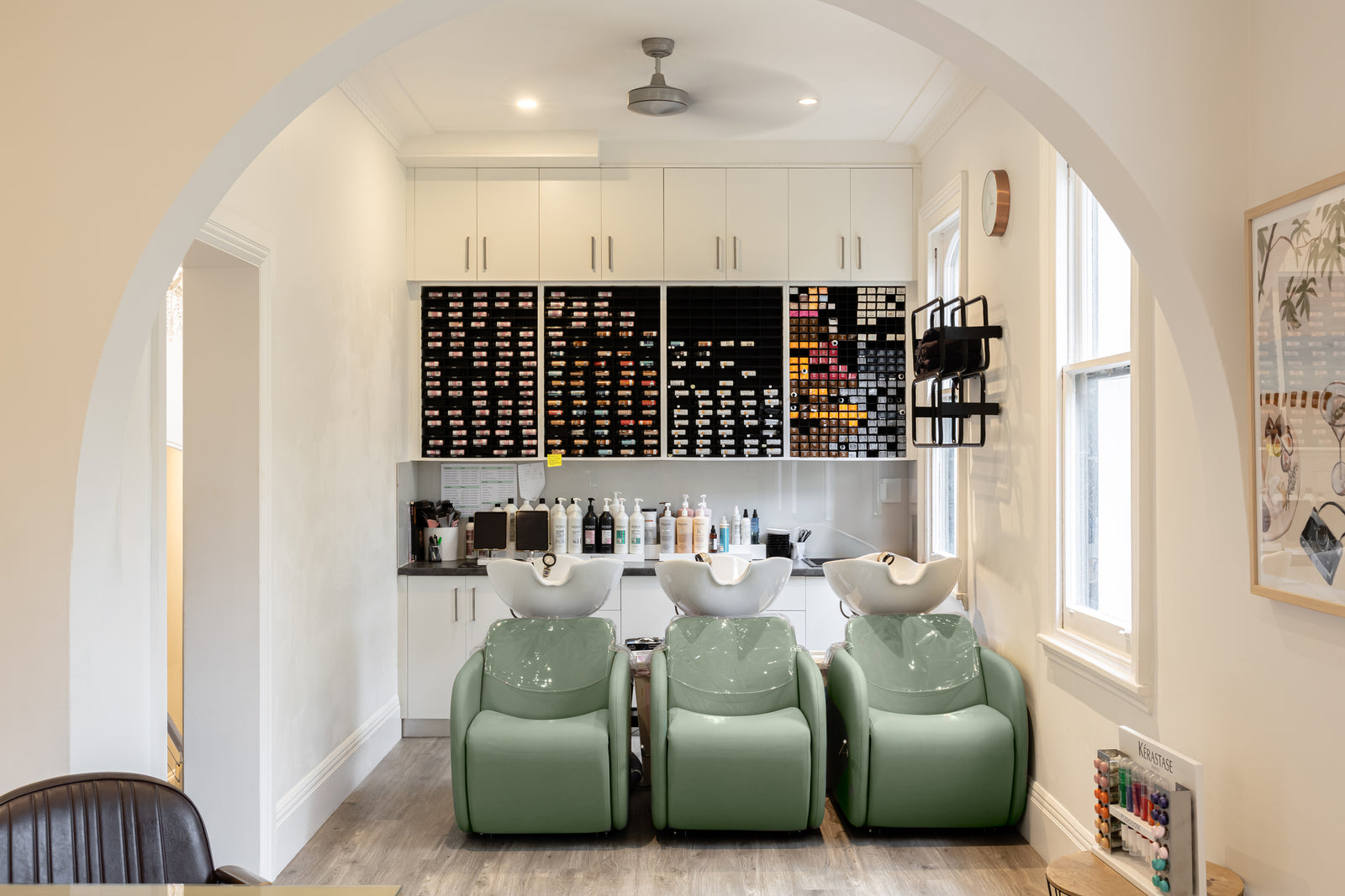 Modern salon interior with green armchairs, colour bar, and white walls.