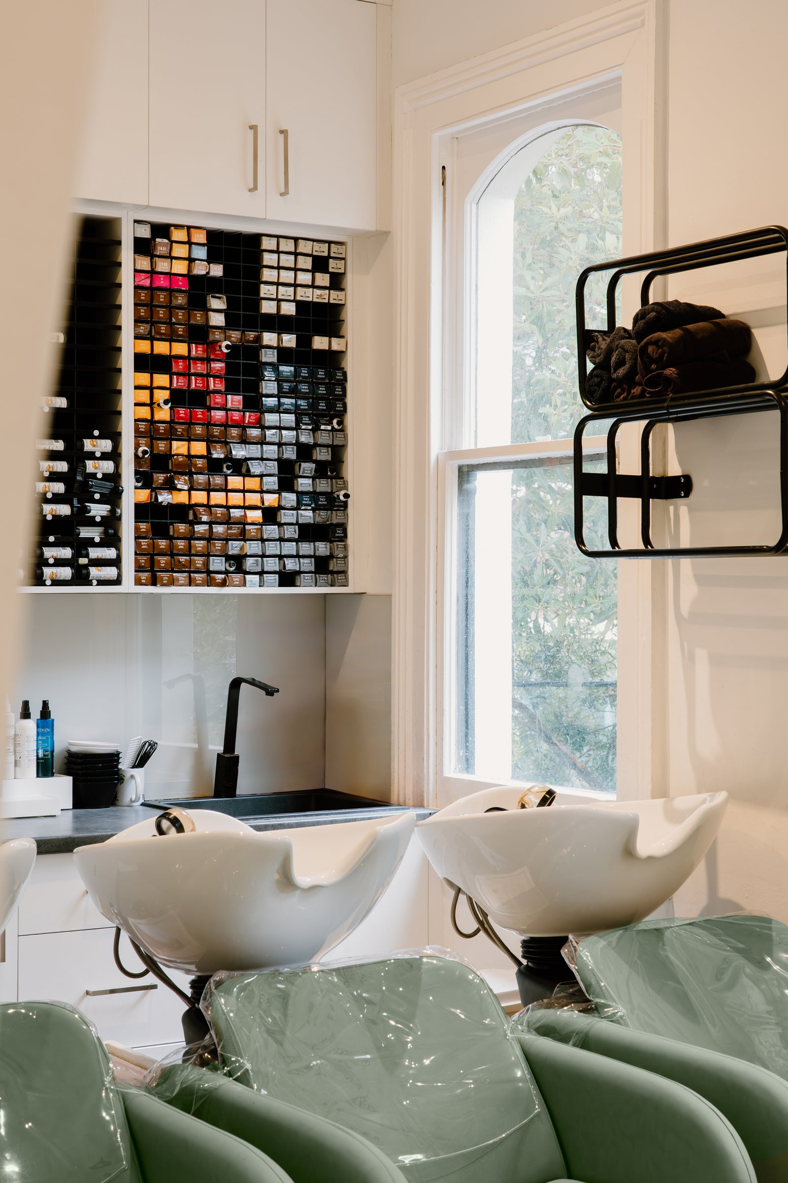 Salon interior with white sinks, green chairs, and a window.
