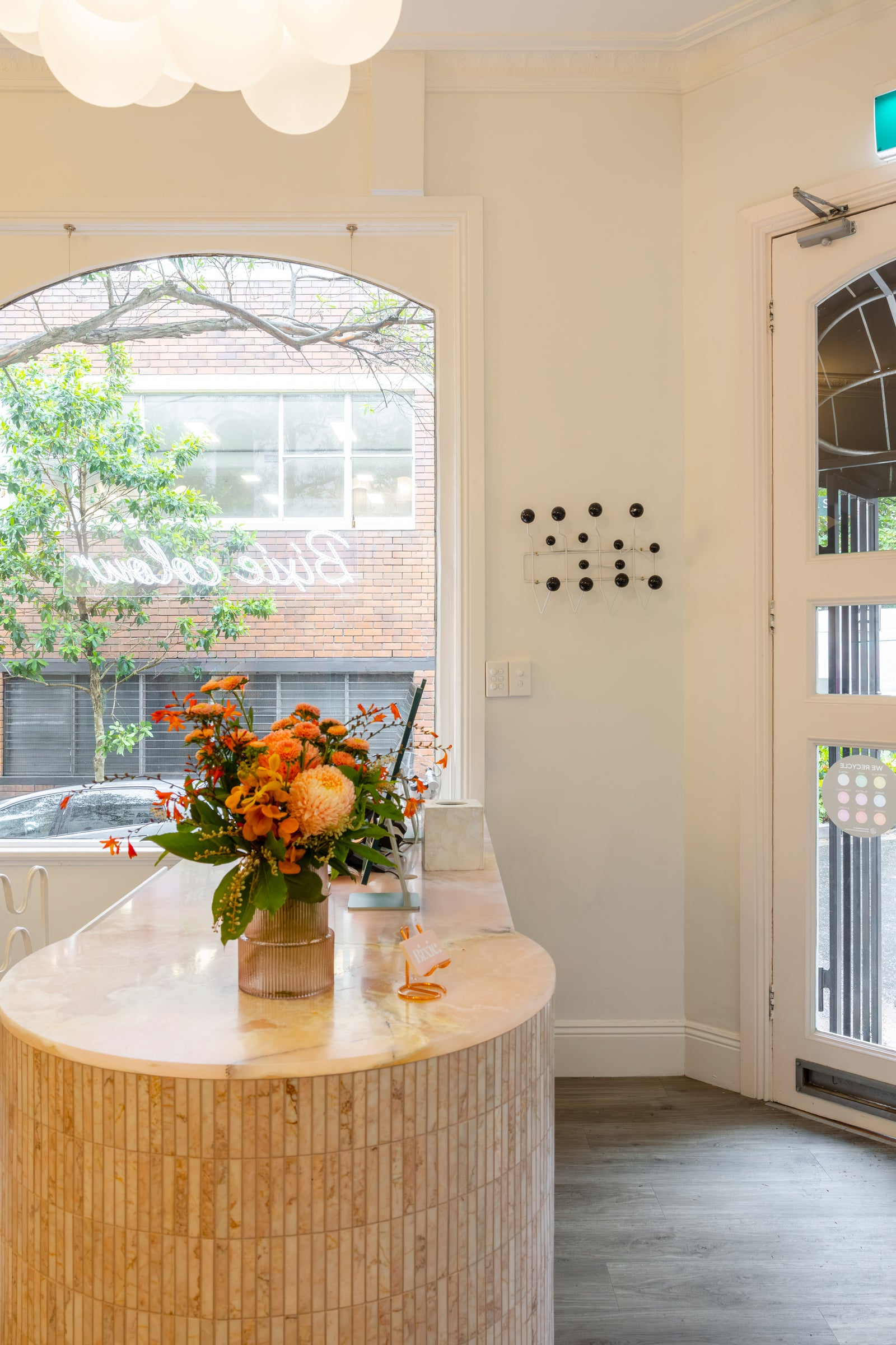 Modern salon interior with a round wooden table and floral arrangement near a window.